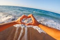 happy young couple showing heart shape with heart shaped hands on sea background, sign at sunrise over sea beach Royalty Free Stock Photo