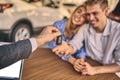 Happy cheerful girl getting a car key with handsome man in showroom. Business concept and car selling Royalty Free Stock Photo