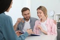 Happy young couple signing purchase contract in estate agent`s office. Man with new house key Royalty Free Stock Photo