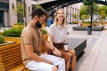 Happy young couple sitting on bench and drinking takeaway coffee enjoying time together outdoors on summer. Royalty Free Stock Photo