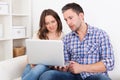 Happy young couple sitting on couch using laptop Royalty Free Stock Photo