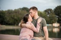 Happy young couple sitting on the dock by the lake, the man kisses the woman on her forehead Royalty Free Stock Photo