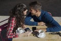 happy young couple sitting on a terrace enjoying a cup of coffee on a sunny day. Using mobile phone and tablet. Outdoors, fun and Royalty Free Stock Photo