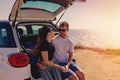 Happy young couple sitting on the trunk of the car