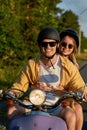 Happy young couple smiling at camera while riding a scooter and having fun at sunset Royalty Free Stock Photo