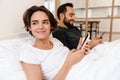 Happy young couple smiling and using mobile phones while lying in bed Royalty Free Stock Photo