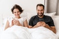 Happy young couple smiling and using mobile phones while lying in bed Royalty Free Stock Photo