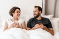 Happy young couple smiling and using mobile phones while lying in bed Royalty Free Stock Photo
