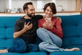 Happy young couple smiling and using mobile phones while sitting on couch Royalty Free Stock Photo