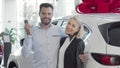 Happy young couple standing near their new car at the dealership Royalty Free Stock Photo