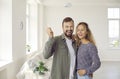 Happy young couple standing in their new house, showing keys to new home and laughing Royalty Free Stock Photo