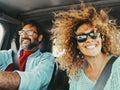 Happy young couple traveling by car together having fun. Woman taking selfie picture in road trip with her husband driving the Royalty Free Stock Photo