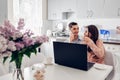 Happy young couple using laptop while having breakfast in modern kitchen. Young man talking on phone Royalty Free Stock Photo