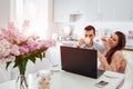 Happy young couple using laptop while having breakfast in modern kitchen. Young man and woman drink coffee and smile Royalty Free Stock Photo