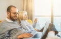 Happy young couple using laptop at home in sunlight. Smiling man holds computer on legs, doing online shopping with his Royalty Free Stock Photo