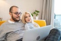 Happy young couple using laptop at home in sunlight. Smiling man holds computer on legs, doing online shopping with his Royalty Free Stock Photo