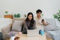 Happy young couple using mobile phone and laptop relax on sofa in living room watch video on laptop together Royalty Free Stock Photo