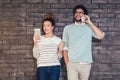 Happy young couple using a tablet and smart phone on a brick wall Royalty Free Stock Photo