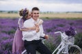 Happy young couple are walking with retro bicycle in lavender field. woman in purple dress and with hairstyle is hugging her man Royalty Free Stock Photo