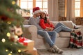 Happy young couple wearing Santa hats on sofa in room decorated for Christmas Royalty Free Stock Photo