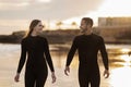 Happy Young Couple Wearing Wetsuits Walking On The Beach At Sunset Time Royalty Free Stock Photo