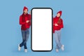 Happy Young Couple Wearing Winter Hats And Scarfs Pointing At Blank Smartphone Royalty Free Stock Photo