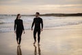 Happy young couple in wetsuits walking on the beach at sunset time Royalty Free Stock Photo