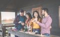 Happy young couples toasting red wine and eating barbecue in backyard wooden house - Cheerful people having fun at sunset in