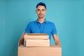 Happy young courier with parcels and envelopes on background