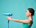Happy young curly brunette woman with hair dryer on blue mint background Royalty Free Stock Photo