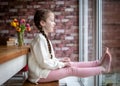 Happy young cute pretty girl with pigtails long hair sat at table indoors looking through window big happy smile and feet up Royalty Free Stock Photo