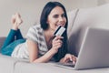 Happy young cute pretty woman showing credit card and doing internet shopping at home on couch Royalty Free Stock Photo