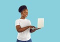 Happy young dark skinned woman smiling typing on laptop isolated on light blue background. Royalty Free Stock Photo