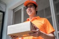 Happy young delivery man in the orange uniform standing with parcel box to send to customers