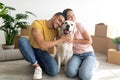 Happy young diverse couple hugging their cute dog, sitting on floor among carton boxes, moving to new home with pet Royalty Free Stock Photo