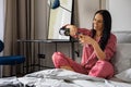 Happy young domestic woman in red pajamas drinking champagne wine glass sitting in comfortable bed Royalty Free Stock Photo