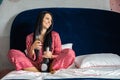 Happy young domestic woman in red pajamas drinking champagne wine glass sitting in comfortable bed Royalty Free Stock Photo