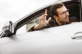 Happy young driver is peeking from the window while waving to someone with his hand. Friendly driver concept