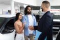 Happy young eastern couple buying new car at dealership salon Royalty Free Stock Photo