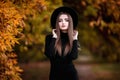 Happy young elegant woman in park on autumn day. Cheerful beautiful girl in black wear and hat outdoors among yellow Royalty Free Stock Photo