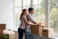 Happy young european guy and woman with cardboard boxes look out panorama window in their own apartment