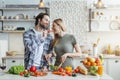 Happy young european husband with stubble feeds woman, lady prepares salad for dinner