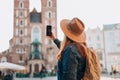 Happy young European tourist with backpack in hat makes photo or video on smartphone on Market Square in Krakow Royalty Free Stock Photo