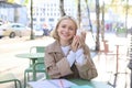 Happy young European woman, drinking coffee, sitting in street cafe, working and chatting, smiling at camera Royalty Free Stock Photo