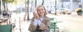 Happy young European woman, drinking coffee, sitting in street cafe, working and chatting, smiling at camera Royalty Free Stock Photo