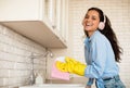 Happy young european woman in headphones washing dishes at home, wearing rubber gloves and enjoying music, copy space Royalty Free Stock Photo