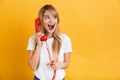 Happy young excited shocked blonde woman posing  over yellow wall background talking by retro red telephone Royalty Free Stock Photo