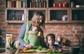 Happy young family, beautiful mother with two children, adorable preschool boy and baby in sling cooking together in a sunny kitch Royalty Free Stock Photo