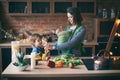 Happy young family, beautiful mother with two children, adorable preschool boy and baby in sling cooking together in a sunny kitch Royalty Free Stock Photo