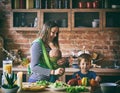 Happy young family, beautiful mother with two children, adorable preschool boy and baby in sling cooking together in a sunny kitch Royalty Free Stock Photo